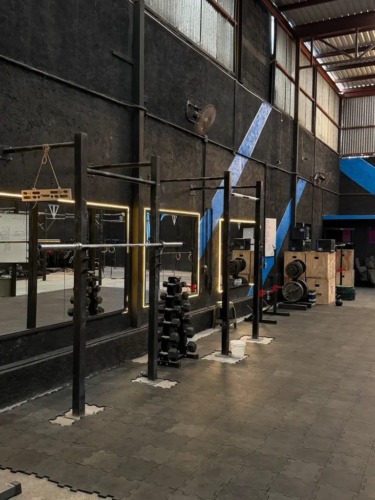 Muro negro con franjas azules diagonales, racks de barras, espejos iluminados y cajones de salto apilados